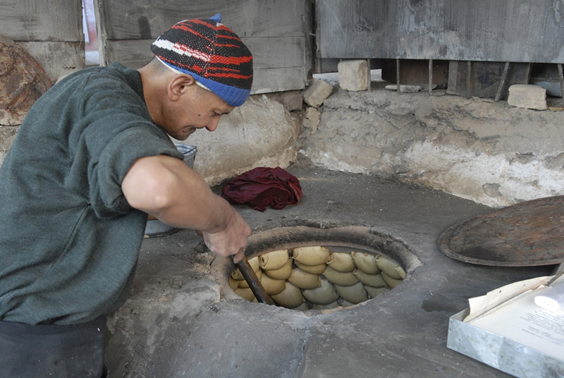 A baker cooks naan, in a traditional tandyr, a style of clay, wood-fired oven used for centuries.